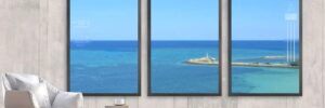 Three large framed windows show a view of the ocean, a small island with a lighthouse, and clear blue sky.