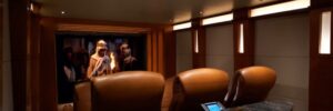A modern home theater room with three leather recliners facing a large screen and a marble-topped counter.