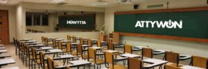 An empty classroom with rows of desks facing a chalkboard and a large mirror reflecting the room; text on board and mirror.
