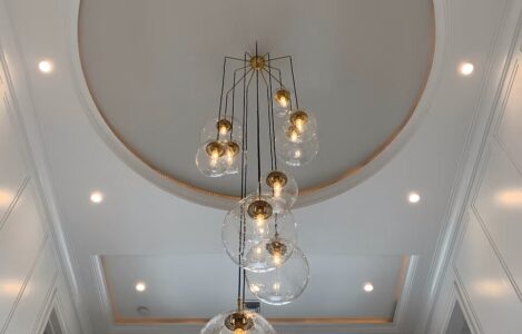 Modern chandelier with multiple glass globes hanging from a high ceiling, surrounded by recessed lighting.