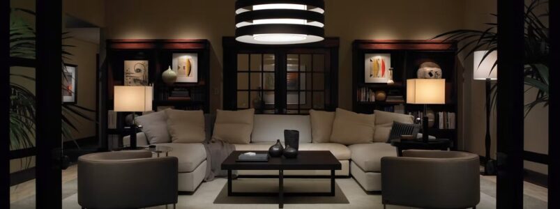 Modern living room with a beige sectional sofa, coffee table, and built-in shelves, softly lit by lamps and a ceiling light.