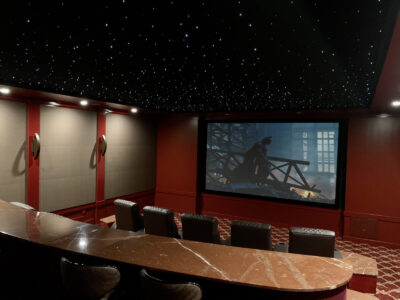 Private home theater with red walls, a marble counter, and a starry ceiling, showing a movie on a large screen.