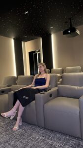 A woman sits alone in a modern home theater room with leather recliners and a starry ceiling effect.