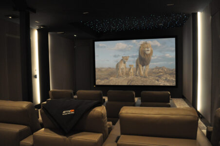 Modern home theater with beige recliners, a large screen displaying lions, and a blanket draped over a front seat.