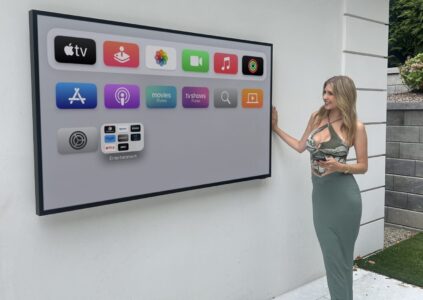 A woman stands beside a large outdoor screen displaying an Apple TV interface with various app icons.