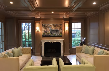 A formal living room with beige sofas, a fireplace, and a deer painting above the mantel.