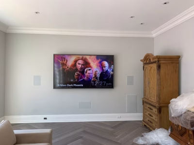 Wall-mounted TV displaying "X-Men: Dark Phoenix" in a minimally furnished room with wooden cabinet and covered furniture.