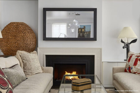 Modern living room with a lit fireplace, neutral sofas, glass coffee table, and contemporary decor elements.