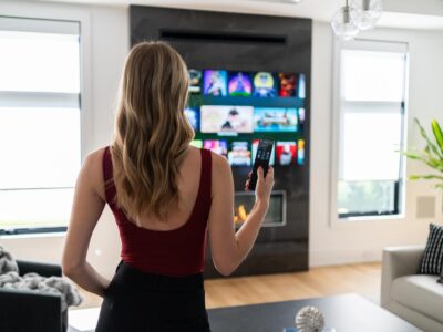 A woman stands in front of a TV holding a remote, browsing streaming options in a modern living room.