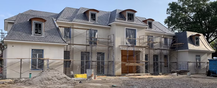 Large two-story house under construction with scaffolding on the exterior and building materials in the front yard.