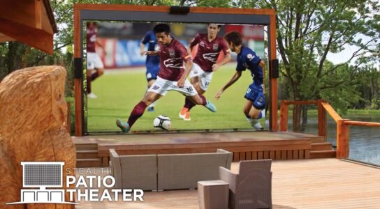 A large outdoor screen on a wooden patio displays a soccer match; chairs face the screen. Text reads "STEALTH PATIO THEATER.